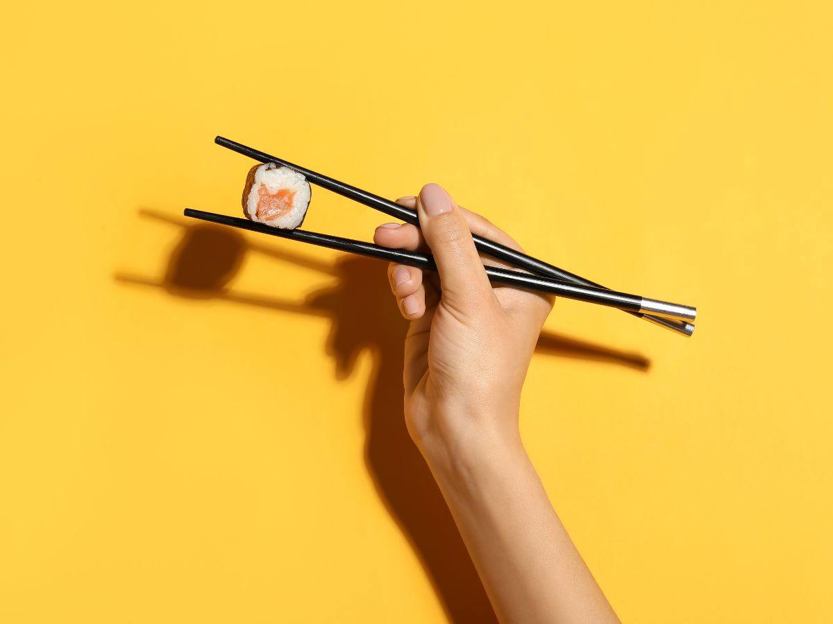 sfondo giallo e mano che tiene sushi con le bacchette